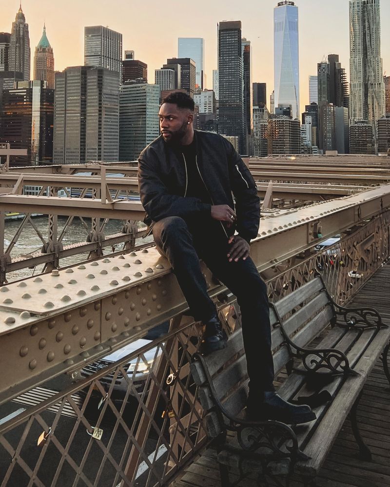 David sitting on the Brooklyn Bridge with the Manhattan skyline behind him